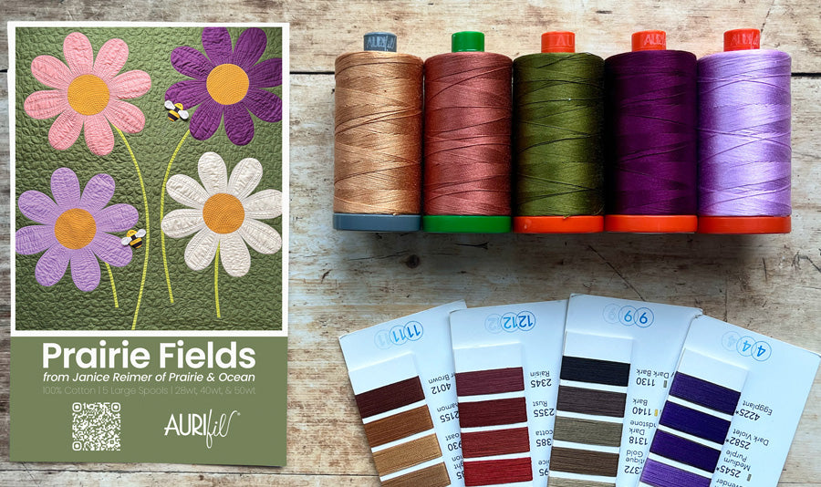 A collection insert with the title 'Prairie Fields' shown next to five spools of thread in earthy and vibrant colors, with Aurifil swatch book cards below, all arranged on a rustic wooden surface.