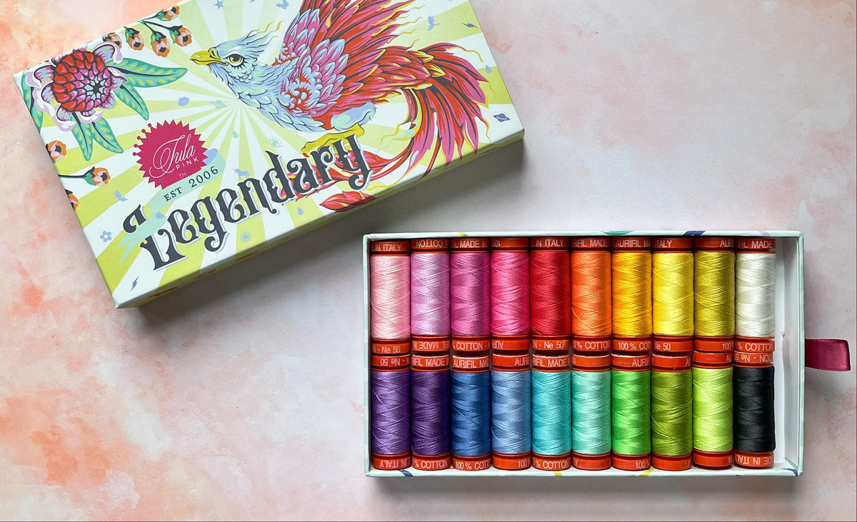 Box of colorful thread spools with a colorful box labeled 'Legendary' on a light pink background.